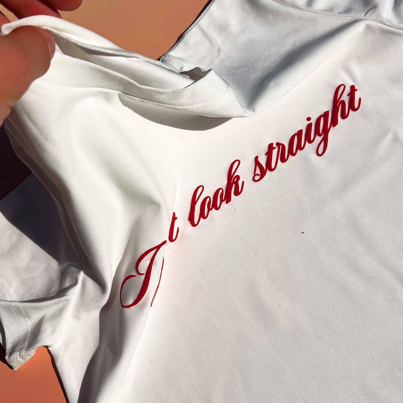 May include: White t-shirt with the text "I't look straight" in red cursive lettering.