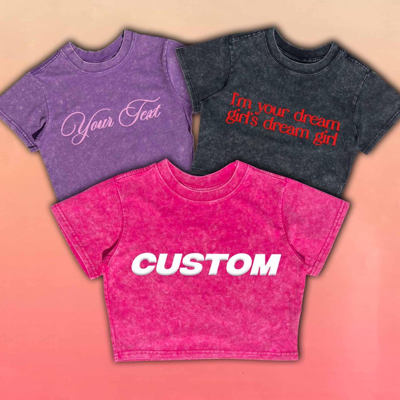May include: Three short-sleeved t-shirts in purple, charcoal, and hot pink. The purple shirt has the text "Your Text" in a cursive font. The charcoal shirt has the text "I'm your dream girl's dream girl" in red. The hot pink shirt has the text "CUSTOM" in white.