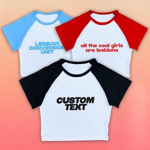 May include: Three white raglan t-shirts with different colored sleeves and text. One has light blue sleeves and reads "LESBIAN CONVERSION UNIT." Another has red sleeves and reads "all the cool girls are lesbians." The third has black sleeves and reads "CUSTOM TEXT."