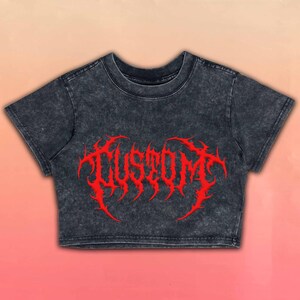 May include: A charcoal gray crop top with a distressed finish. The shirt features the word "CUSTOM" in a bold, red, gothic-style font across the front. The background has a gradient of pink and peach.