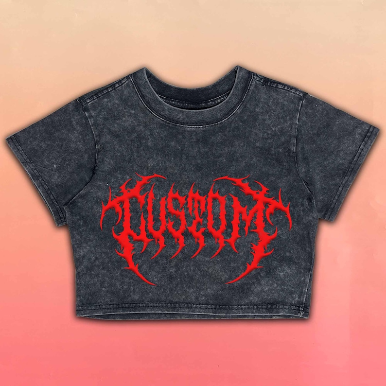 May include: A charcoal gray crop top with a distressed finish. The shirt features the word "CUSTOM" in a bold, red, gothic-style font across the front. The background has a gradient of pink and peach.