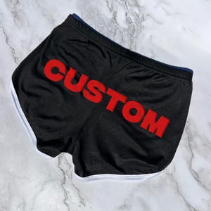 May include: Black athletic shorts with a white trim and the word "CUSTOM" in red lettering.