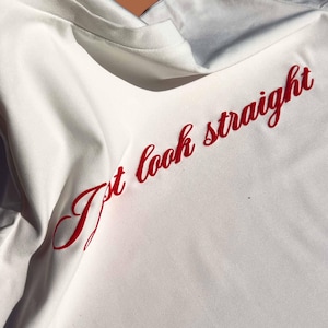 May include: White t-shirt with the text "I't look straight" in red cursive lettering.