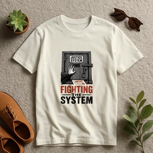 Könnte beinhalten: Ein cremefarbenes T-Shirt mit einer Grafik einer Hand, die nach einer verschlossenen Tür mit der Aufschrift JUSTICE SYSTEM greift. Unter der Tür liegt ein Dokument mit der Aufschrift LAWSUIT und der Text FIGHTING THE SYSTEM.