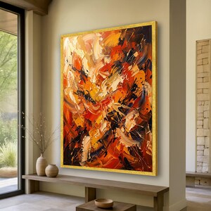 May include: Large abstract painting with a gold frame. The artwork features bold brushstrokes in shades of orange, red, black, and white, creating a dynamic and textured composition. The painting is displayed in a well-lit room.