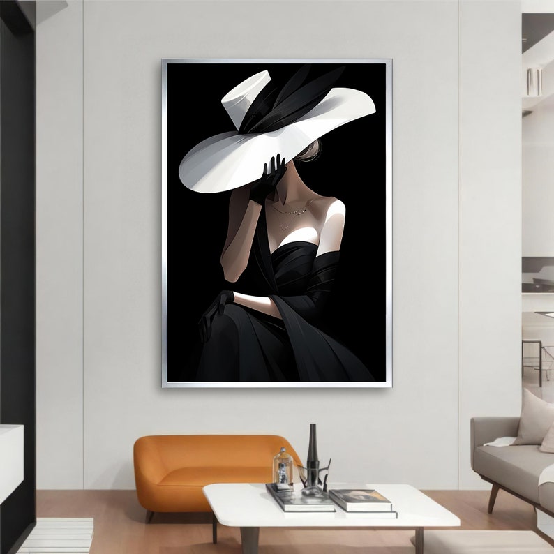Peut inclure: Une femme en robe noire et un grand chapeau blanc pose sur un fond noir. Le chapeau lui couvre le visage et elle porte un collier.