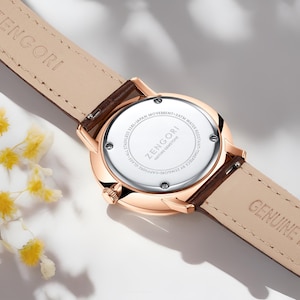 Puede incluir: Un reloj de oro rosa con una correa de cuero marr&oacute;n. La parte posterior del reloj tiene el texto "ZENGORI" y "NATURE GEMSTONE" impreso. El reloj es resistente al agua hasta 3 ATM.