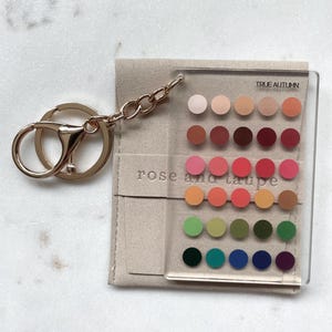 May include: A clear rectangular acrylic keychain featuring a grid of thirty colored circles in various shades. The text TRUE AUTUMN and rose and taupe are printed on the surface. It includes a gold-toned metal ring and chain.
