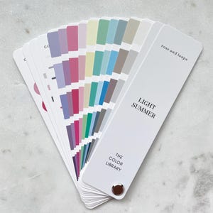 May include: A fan-shaped color swatch deck titled LIGHT SUMMER and THE COLOR LIBRARY, with the text rose and taupe. The deck features multiple cards displaying various shades of pink, purple, blue, green, yellow, and gray in a gradient.