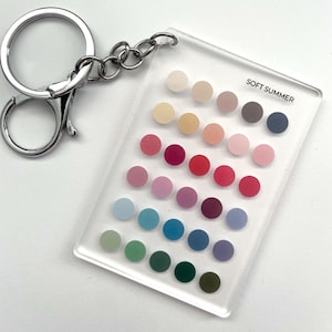May include: A clear acrylic keychain with a silver metal ring and chain. The keychain features a rectangular panel with a grid of colorful dots in shades of pink, blue, green, and purple. The text "SOFT SUMMER" is printed on the panel.