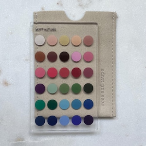 May include: A clear rectangular acrylic card featuring a grid of thirty colored circles, labeled SOFT AUTUMN at the top. The card rests on a beige fabric pouch with the text rose and taupe printed vertically along the right side.