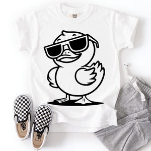 May include: White t-shirt featuring a black and white graphic of a duck wearing sunglasses. The image also shows a pair of black and white checkered slip-on shoes and gray sweatpants.