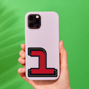 May include: A white phone case with a red and black sticker of the number one on it.