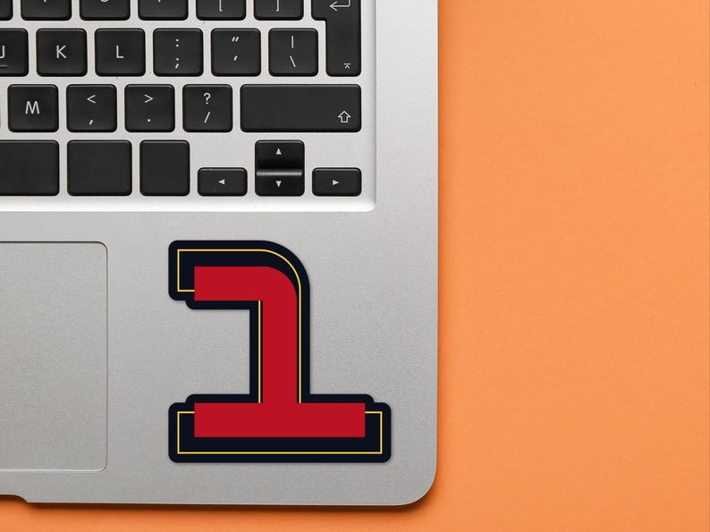 May include: A red and black number one sticker on a silver laptop. The number one is outlined in black and has a gold outline.