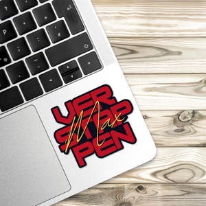 May include: A red and black sticker with the text "VER STAPPEN" in yellow lettering. The sticker is on a silver laptop.