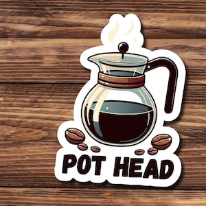 May include: A white sticker with a cartoon illustration of a coffee pot with steam coming out of the spout. The pot is filled with coffee and there are coffee beans scattered around it. The text "POT HEAD" is written below the pot.