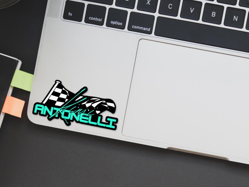 May include: A sticker featuring a checkered racing flag design with the name "Antonelli" in a teal font. The sticker is placed on a laptop, with a black background visible.