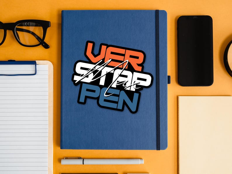 May include: A blue notebook with a sticker that says "VER STAP PEN" in white, orange, and blue lettering. The notebook is on a yellow surface with a pen, a notepad, and a smartphone.