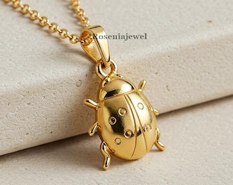 Puede incluir: Un collar de tono dorado con un colgante de mariquita que presenta detalles circulares grabados. El colgante está unido a una delicada cadena de tono dorado. El texto "Roseniajewel" es visible en el colgante. El diseño es pulido y metálico.