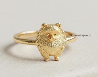 May include: A gold-colored ring featuring a Pomeranian dog design. The dog is standing upright with detailed fur and facial features. The ring band is smooth and simple, with the brand name "Roseniajewel" visible on the side.