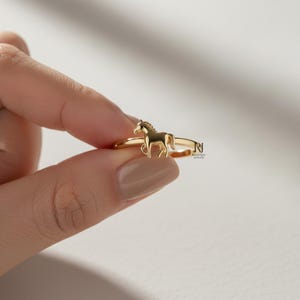 May include: A gold-colored ring featuring a detailed horse figure. The ring has a thin band and a small horse silhouette as the focal point. The jewelry is displayed against a neutral background.