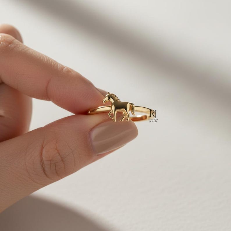 May include: A gold-colored ring featuring a detailed horse figure. The ring has a thin band and a small horse silhouette as the focal point. The jewelry is displayed against a neutral background.