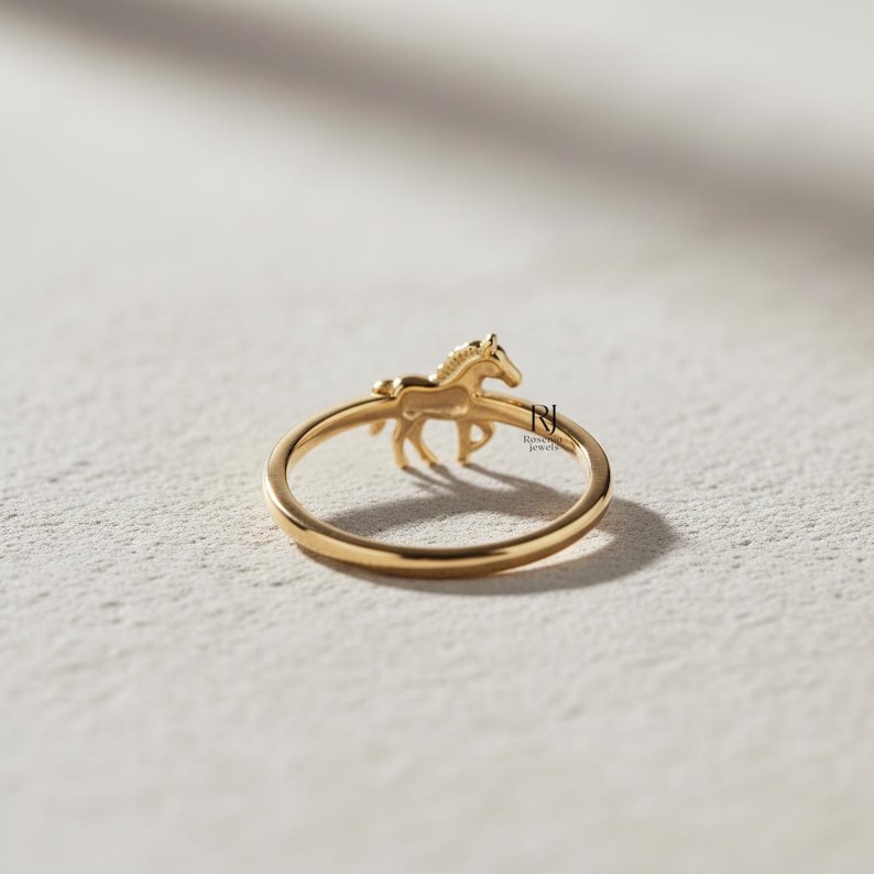 May include: A gold-colored ring featuring a detailed horse figure. The horse is positioned on the ring's band, with its legs and body visible. The ring has a polished finish and is set against a neutral background.