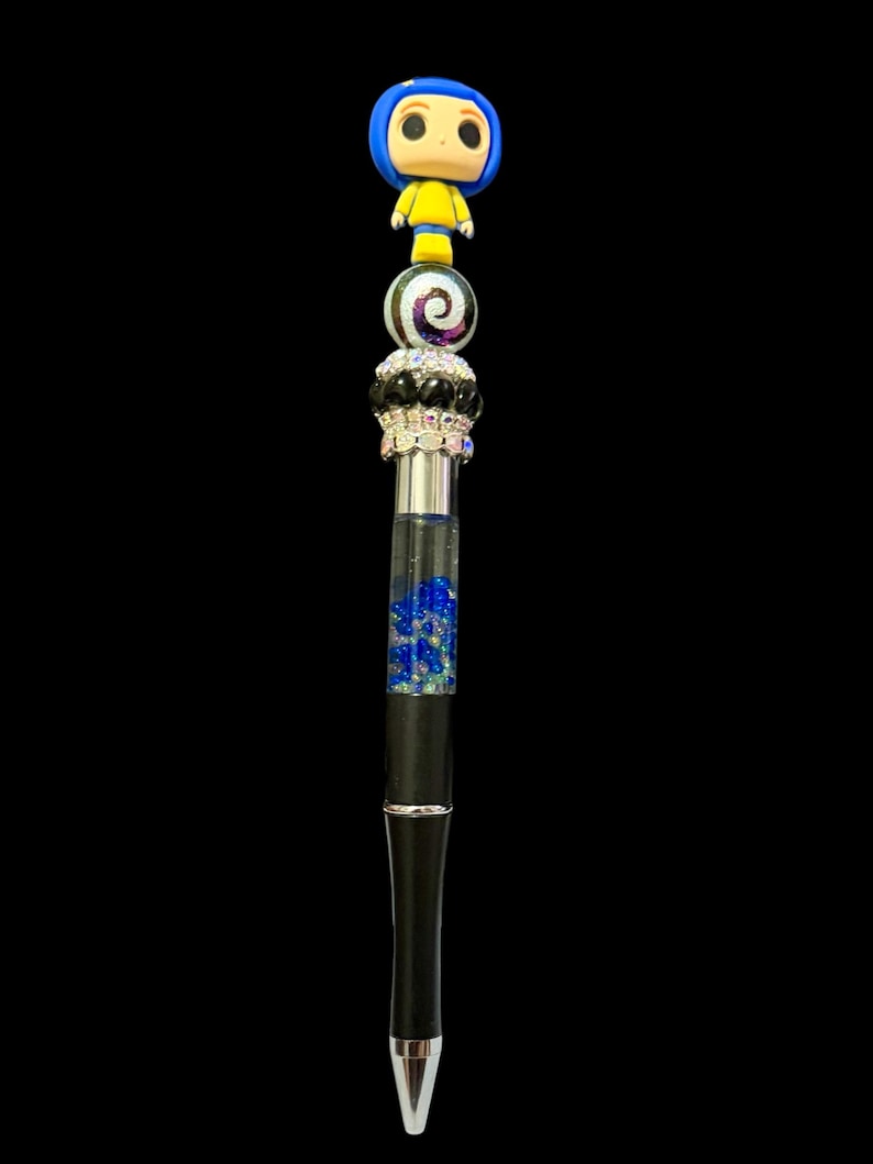 May include: A decorative pen featuring a figurine of a character with blue hair and yellow clothing. The pen has a black barrel, a silver and black decorative section, and a clear section filled with blue glitter. The pen is set against a black background.