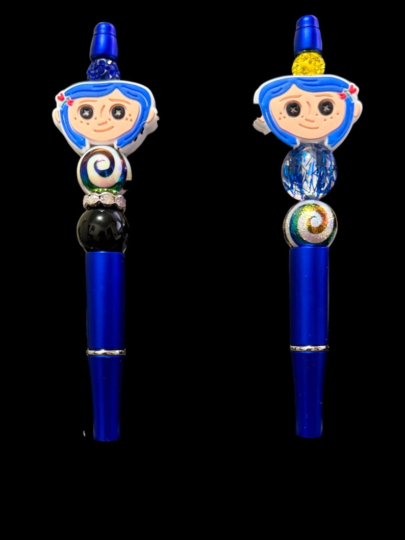 May include: Two blue pens with decorative tops featuring a cartoon character with blue hair and a white face. The pens have a series of colorful beads and a silver band. The background is black.
