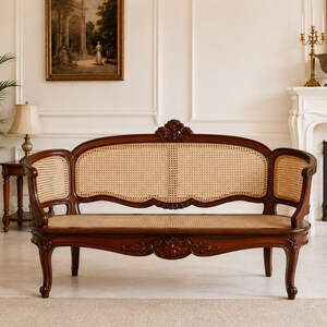 May include: A dark wood settee featuring a curved backrest and seat panel made of woven light tan cane. The frame displays intricate carved floral details on the top center and front apron, supported by four curved legs with a polished finish.