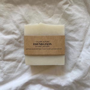 May include: A rectangular bar of off-white soap wrapped in a brown paper label. The label features the text TALLOW & FORM FOUNDATION, unscented pure tallow, and a list of ingredients including rendered beef tallow, coconut oil, water, and sodium hydroxide.