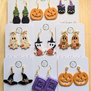 May include: A collection of eight pairs of Halloween-themed polymer clay earrings on white display cards. Designs include green smoke in black cauldrons, orange jack-o'-lanterns, black cats with purple hats, floral ghosts, ghosts with brooms, patchwork ghosts, witch hats, and purple spell books.