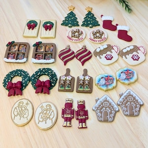May include: A collection of Christmas-themed decorative items, including miniature Christmas trees, wreaths, gingerbread houses, nutcrackers, and ornaments. The items feature red, green, white, and gold colors, with some displaying the text "Santa's Cookies".