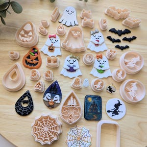 May include: A collection of Halloween-themed cookie cutters in various shapes, including ghosts, bats, pumpkins, and spiderwebs. The cutters are in shades of beige, black, orange, and blue, perfect for creating festive treats.