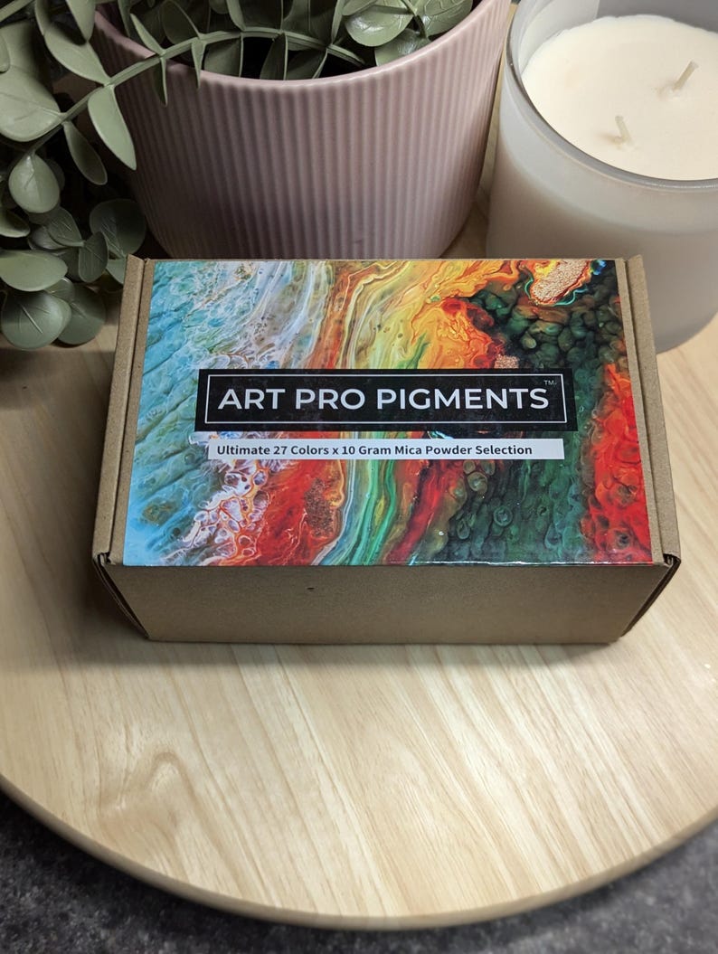 May include: A cardboard box with a colorful abstract design on the top. The box is labeled "ART PRO PIGMENTS" and "Ultimate 27 Colors x 10 Gram Mica Powder Selection".