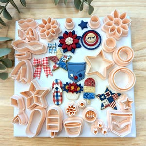 May include: A collection of peach-colored plastic cookie cutters in various shapes including stars, flowers, bows, and pockets, alongside several finished decorative pieces featuring red, white, and blue patterns and the text 1776 on a circular emblem.