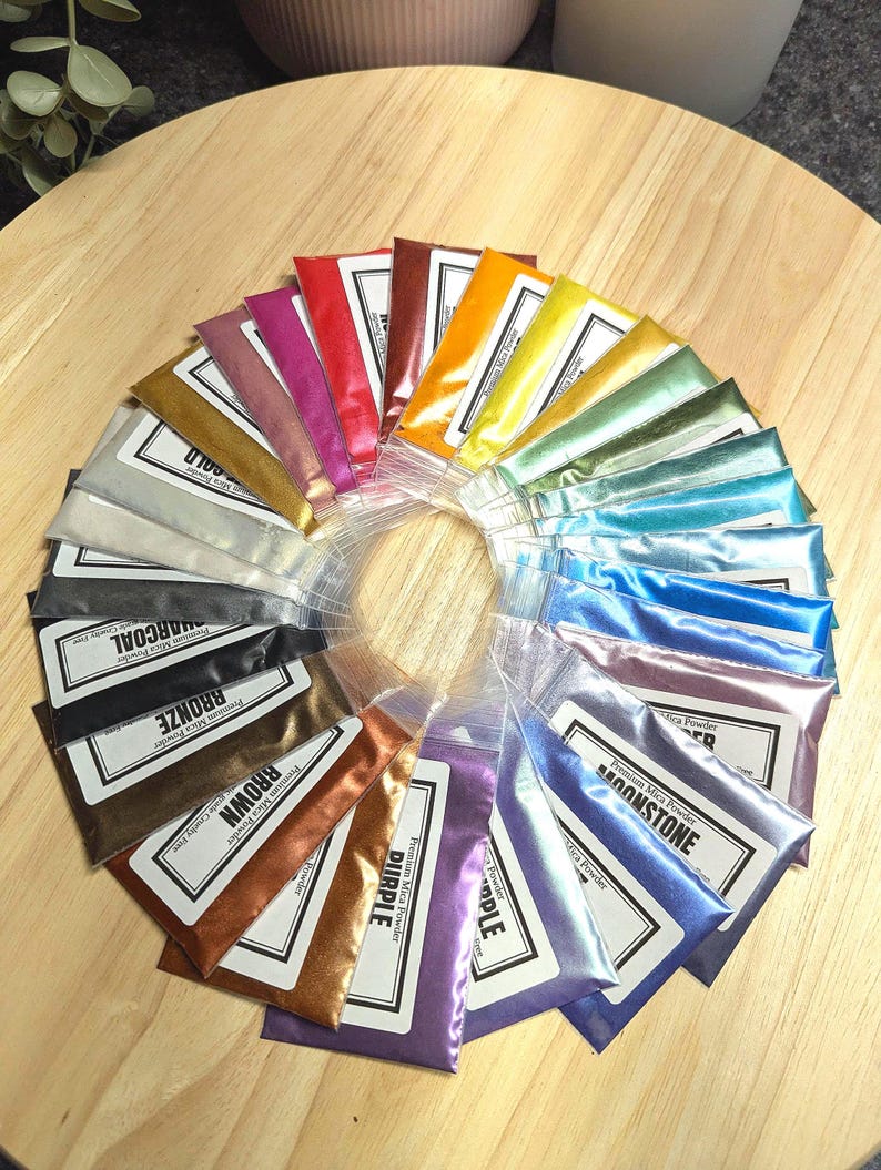 Packets of Mica Powder in 27 vibrant colors are displayed on a natural wood tray. Metallic and Pearlescent shades shimmer in the light