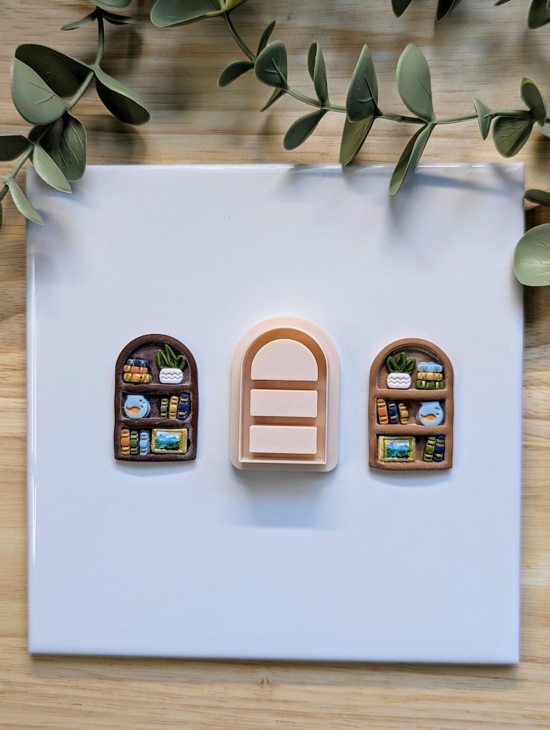 Puede incluir: Tres cortadores de arcilla polim&eacute;rica con forma de estanter&iacute;a. Dos est&aacute;n detallados con libros en miniatura, plantas y obras de arte. El tercero es una forma de arco simple con tres l&iacute;neas horizontales. Los cortadores son marrones, beige y de varios colores.