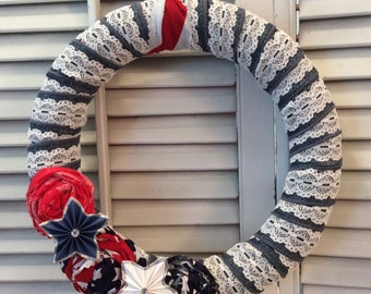 May include: A patriotic wreath made with blue and white striped fabric and white lace. The wreath is decorated with red, white, and blue fabric flowers and a white star.