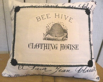 May include: A white pillow with black trim and a black and white image of a beehive with the text "Bee Hive Clothing House" printed on it.