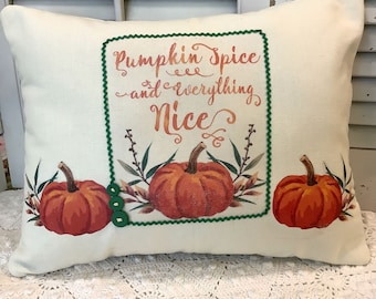 May include: A white pillow with a green border and the text "Pumpkin Spice and everything Nice" in brown lettering. The pillow features three orange pumpkins with green stems and leaves.