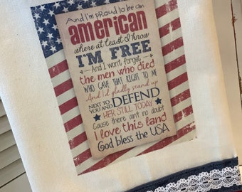 May include: A white canvas tote bag with a red, white, and blue American flag design. The bag features a printed message that reads "And I'm proud to be an american where at least I know I'M FREE - And I won't forget the men who died WHO GAVE THAT RIGHT TO ME And I'd gladly stand up NEXT TO DEFEND YOU AND HER STILL TODAY Cause there ain't no doubt I love this land God bless the USA".