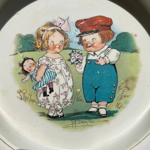 May include: A vintage ceramic plate with a hand-painted illustration of two children. The girl is holding a doll and the boy is offering a bouquet of flowers. The plate is signed "G.G. Drayton".