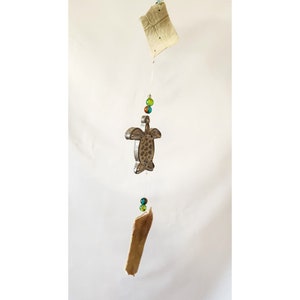 May include: A wooden turtle wind chime with brown and green glass beads hanging from it. The turtle is painted silver and has a detailed design. The wind chime is hanging from a white ceiling.
