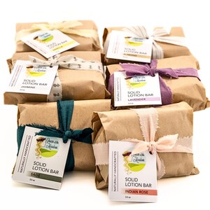 May include: An assortment of handcrafted solid lotion bars, wrapped in brown paper and tied with various colored ribbons. Each bar is labeled with a different scent, including Jasmine, Sage, Lavender, and Indian Rose. The bars are 3.5 oz each.