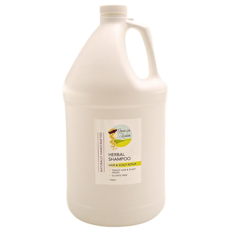 K&ouml;nnte beinhalten: Ein wei&szlig;er Plastik-Gallonenkanister mit Kr&auml;uter-Shampoo zur Reparatur von Haar und Kopfhaut. Das Etikett ist gr&uuml;n und gelb mit dem Gesicht einer Frau und dem Text "Queen of the Meadow" und "Herbal Shampoo".