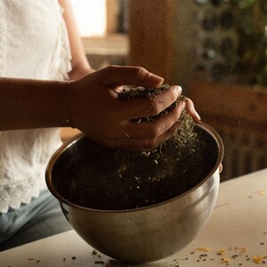 K&ouml;nnte beinhalten: Eine Hand sch&uuml;ttet getrocknete Kr&auml;uter in eine Sch&uuml;ssel aus Edelstahl. Die Kr&auml;uter sind hellbraun und liegen verstreut um die Sch&uuml;ssel herum.