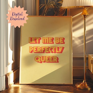 May include: A yellow and red print with the text "Let me be perfectly queer" in a retro font style. The print is framed in gold and is sitting on a wooden floor.