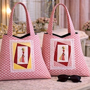 Op de afbeelding: Twee roze draagtassen met een wit bloemenpatroon en zwarte handvatten. Elke tas heeft een ingelijste afbeelding van een vrouw in een rode jurk en hoed. Een zwarte zonnebril ligt voor de tassen.