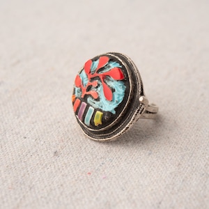 Pode incluir: Um anel de prata com um design redondo de esmalte colorido. O design apresenta um fundo azul com detalhes vermelhos, amarelos e roxos.
